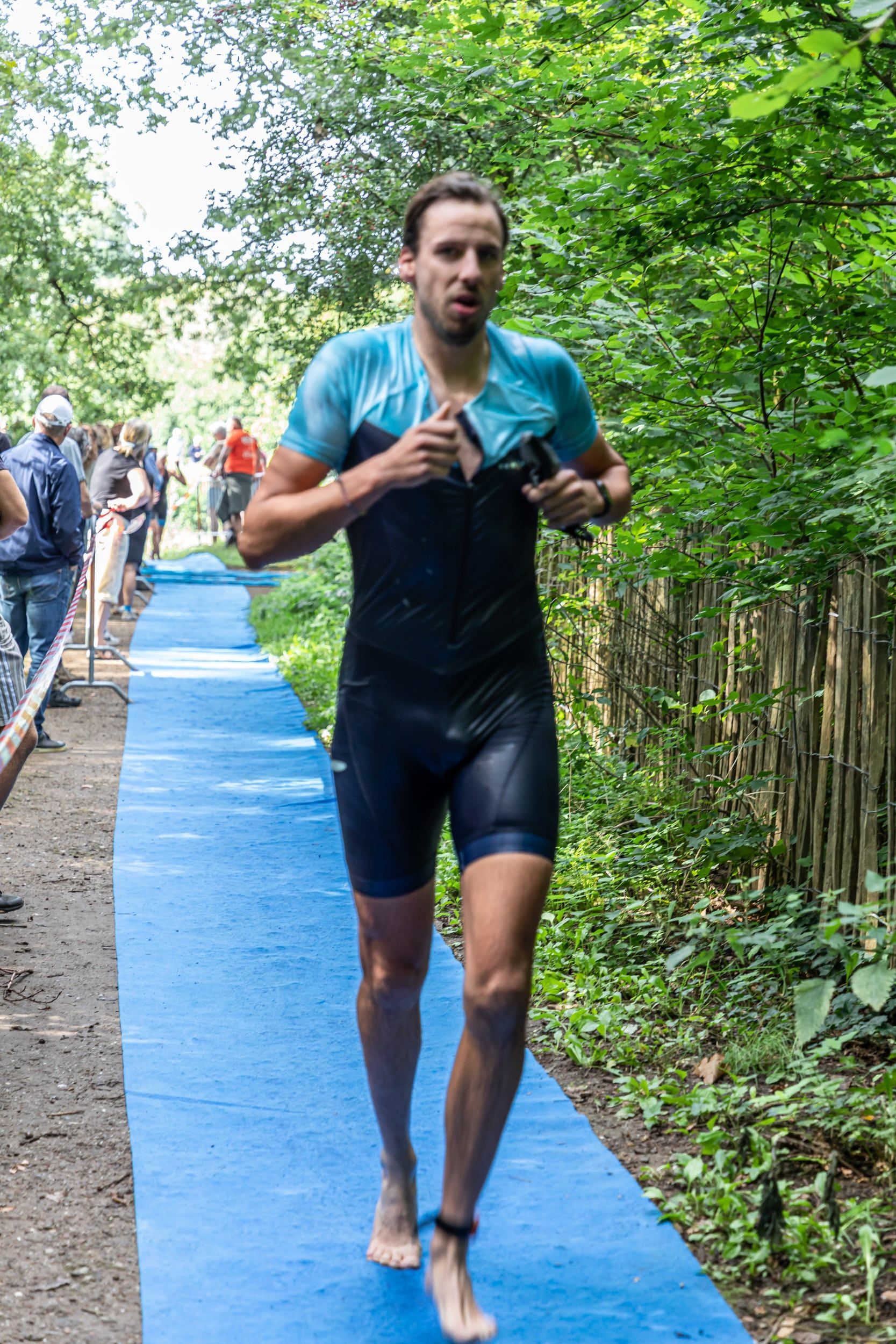 Een man in een wetsuit rent op een blauw pad in het bos.