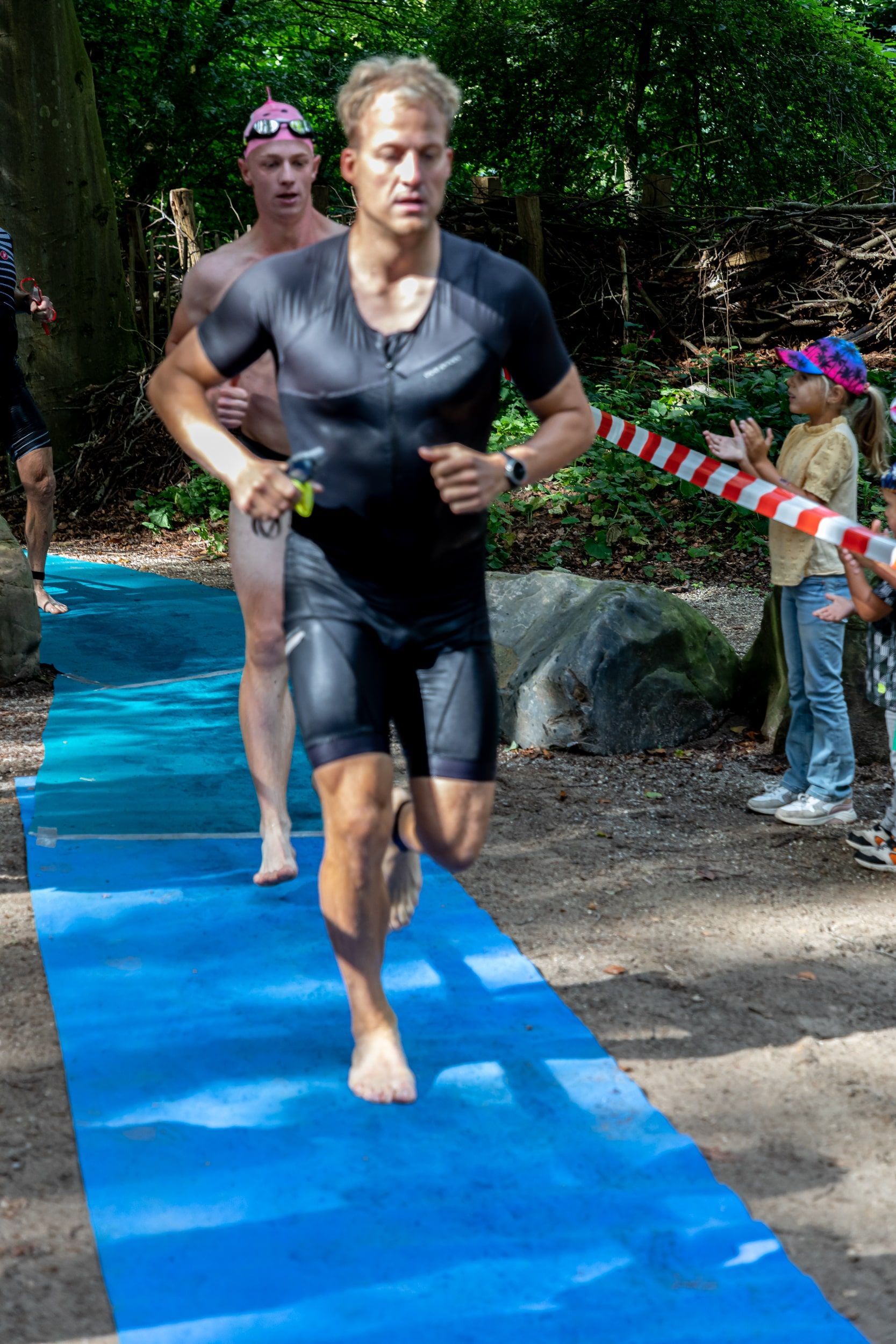 Een man in een wetsuit rent op een blauwe mat.