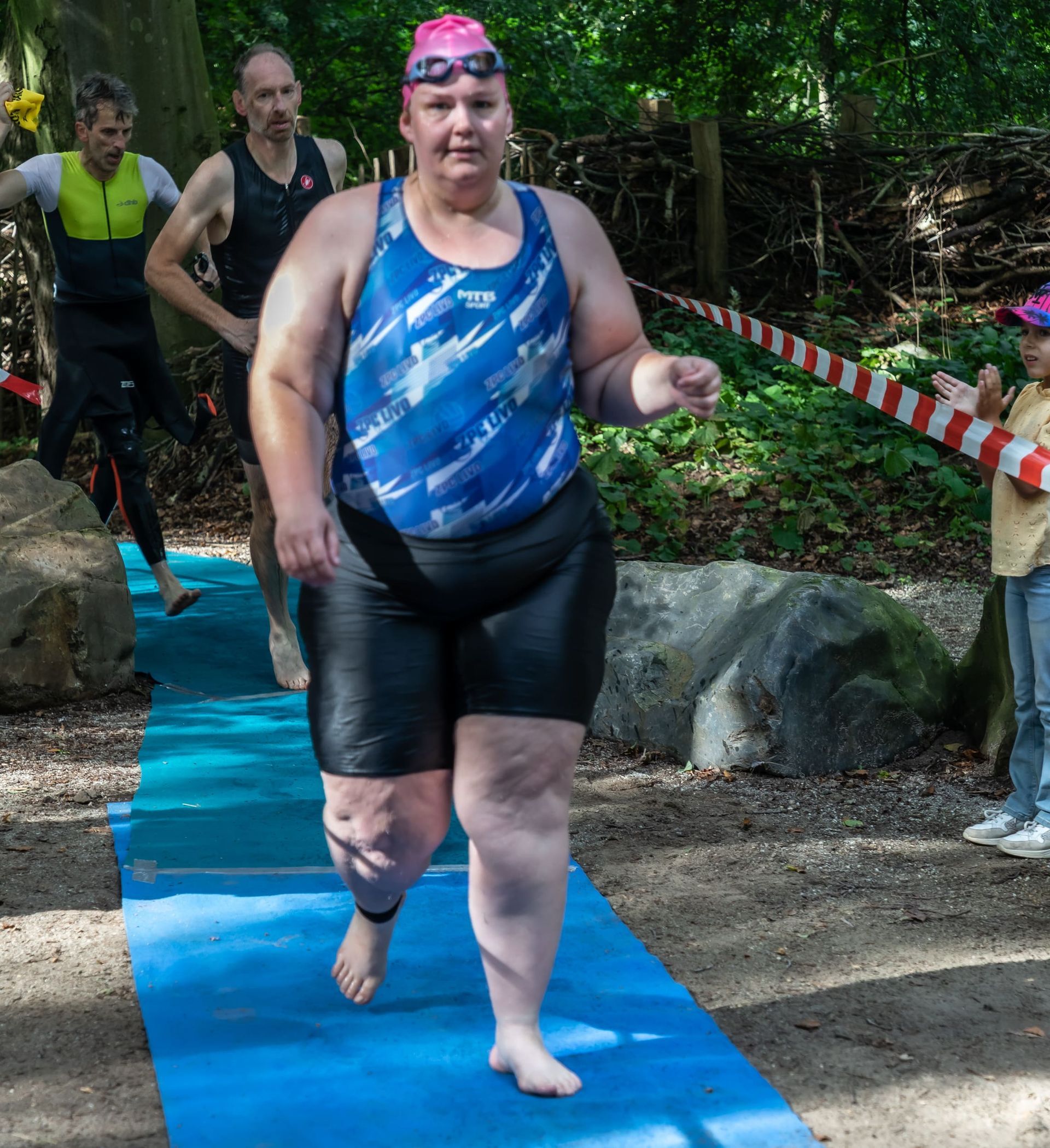 Een vrouw in een blauw tanktopje en zwarte shorts rent op een blauwe mat