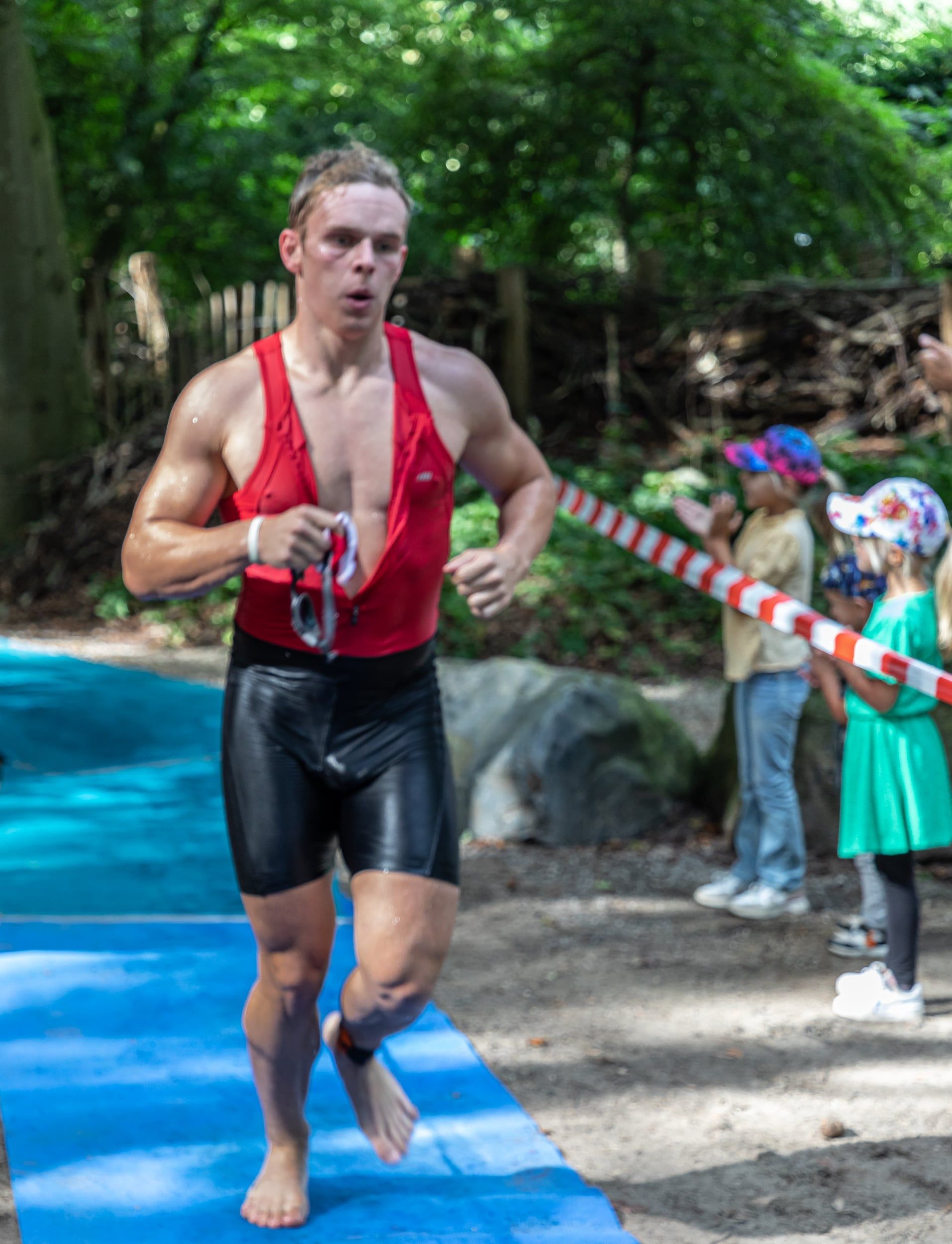 Een man in een rood tanktopje en een zwarte korte broek rent op een blauwe mat.