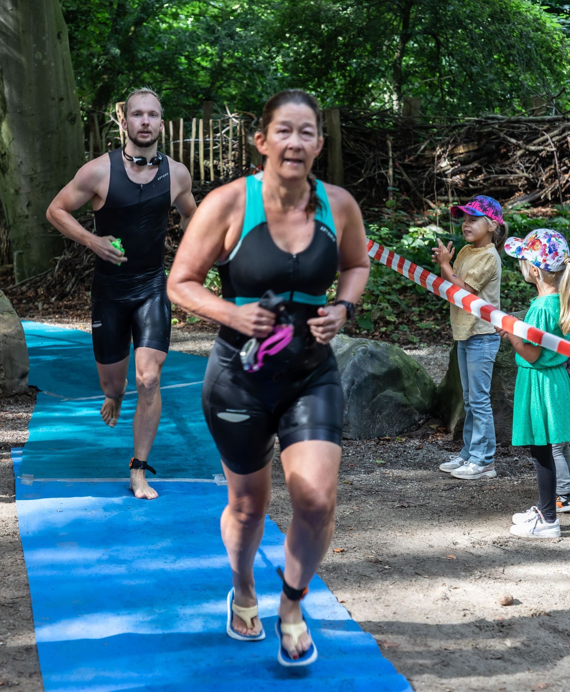 Een man en een vrouw rennen op een blauwe mat in het bos.