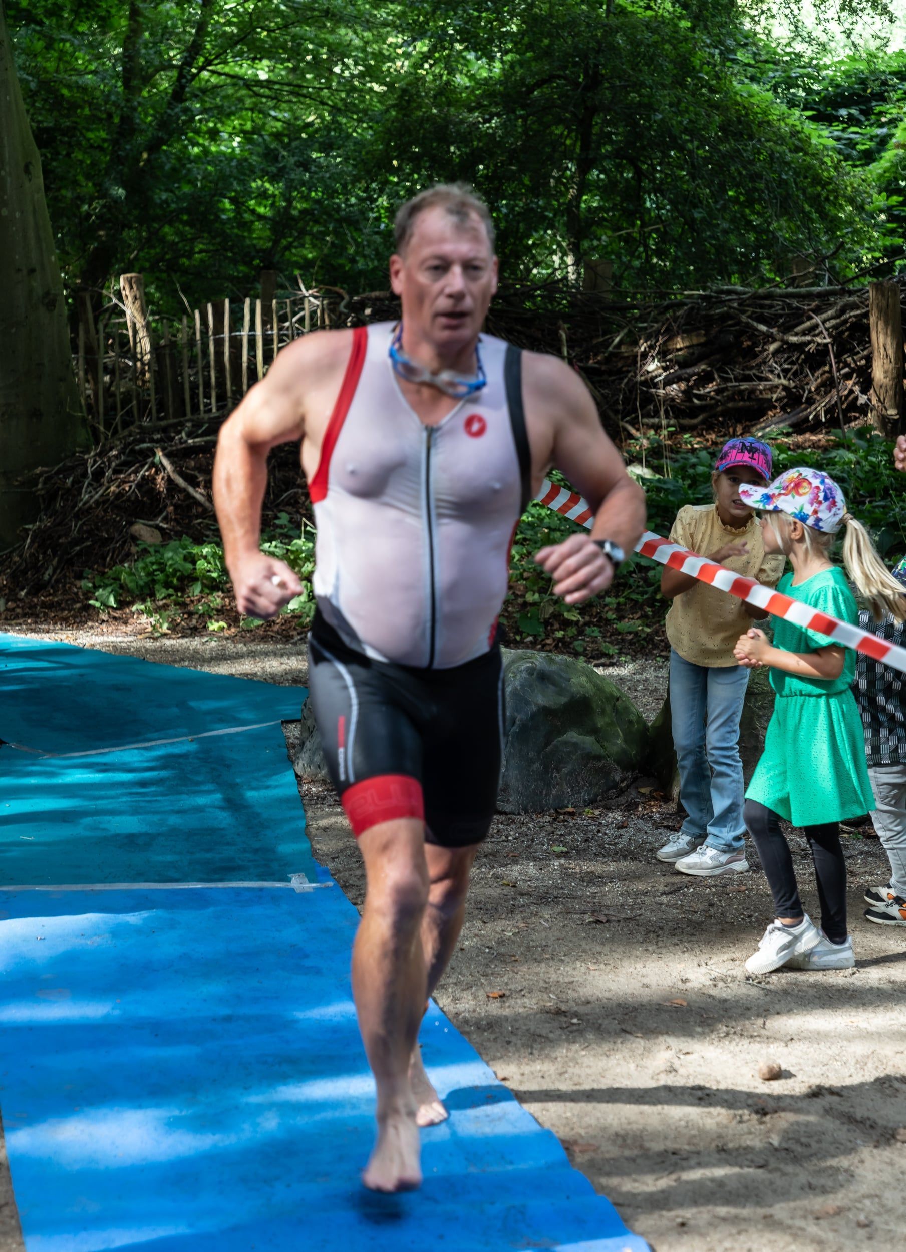 Een man in een triatlonpak rent op een blauwe mat