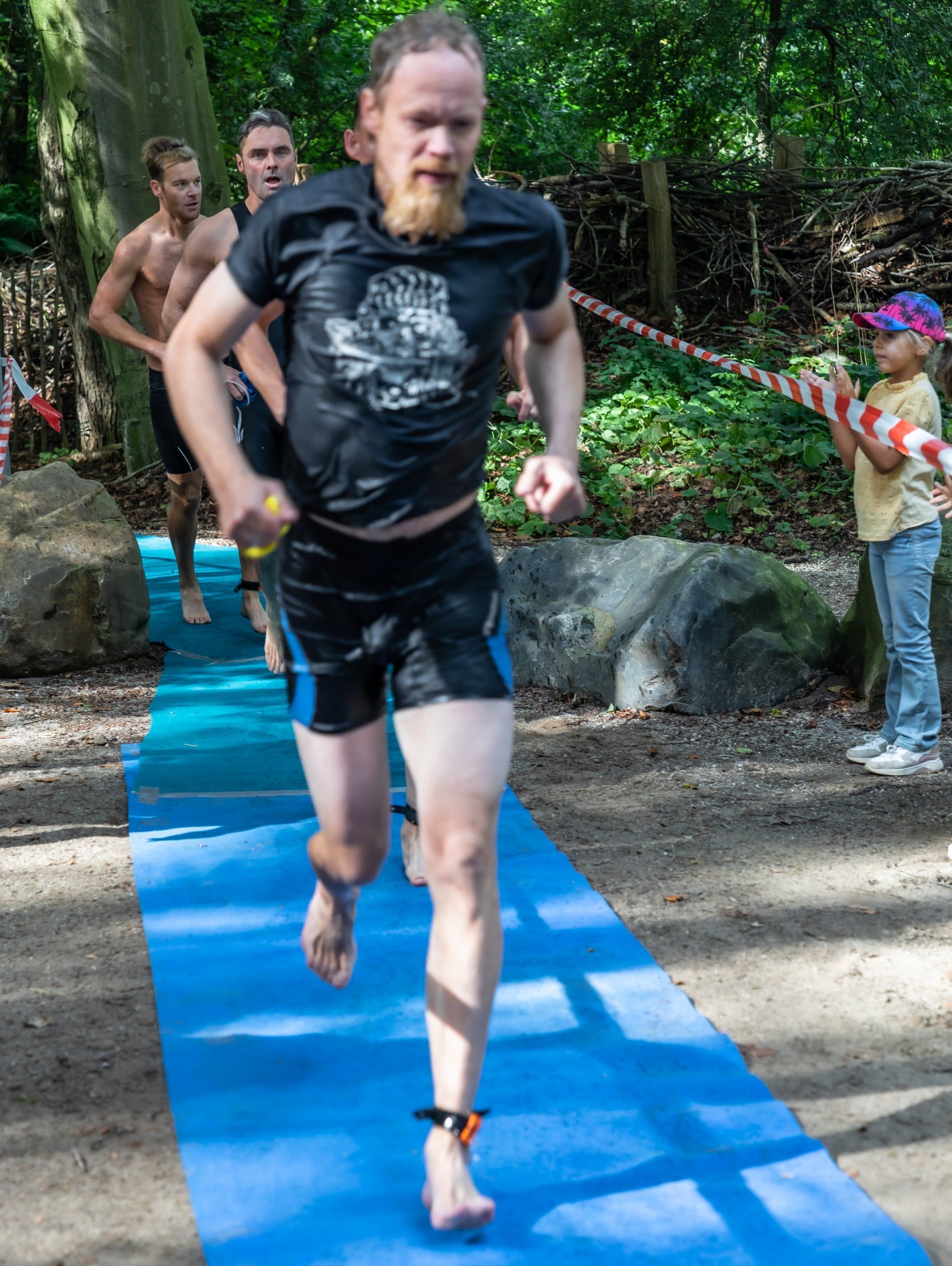 Een man met een baard rent op een blauwe mat in het bos.