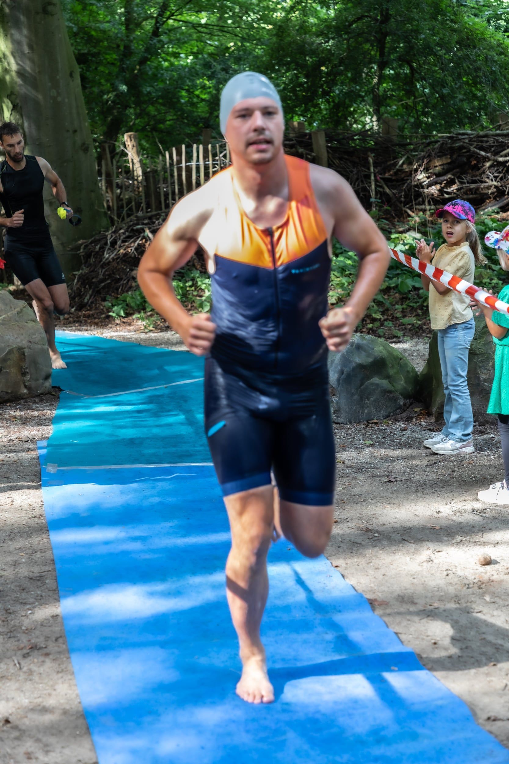 Een man met een badmuts rent op een blauwe mat.