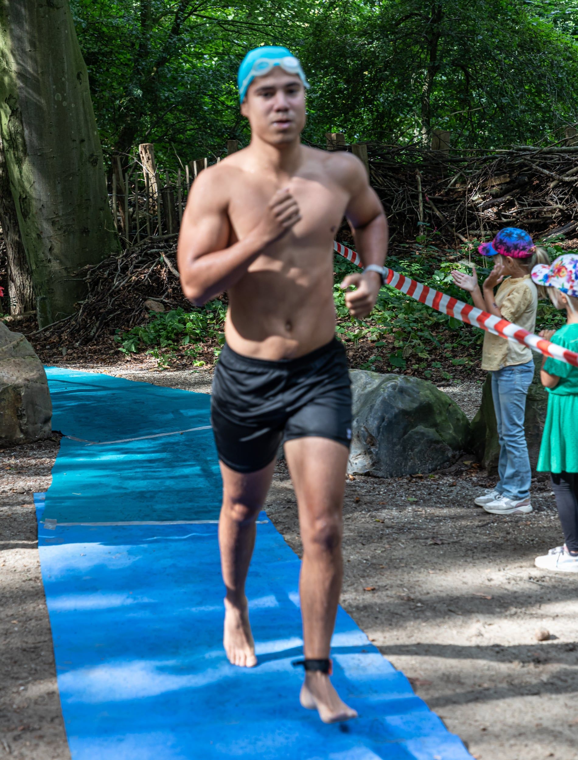 Een man zonder shirt rent op een blauwe mat in het bos.