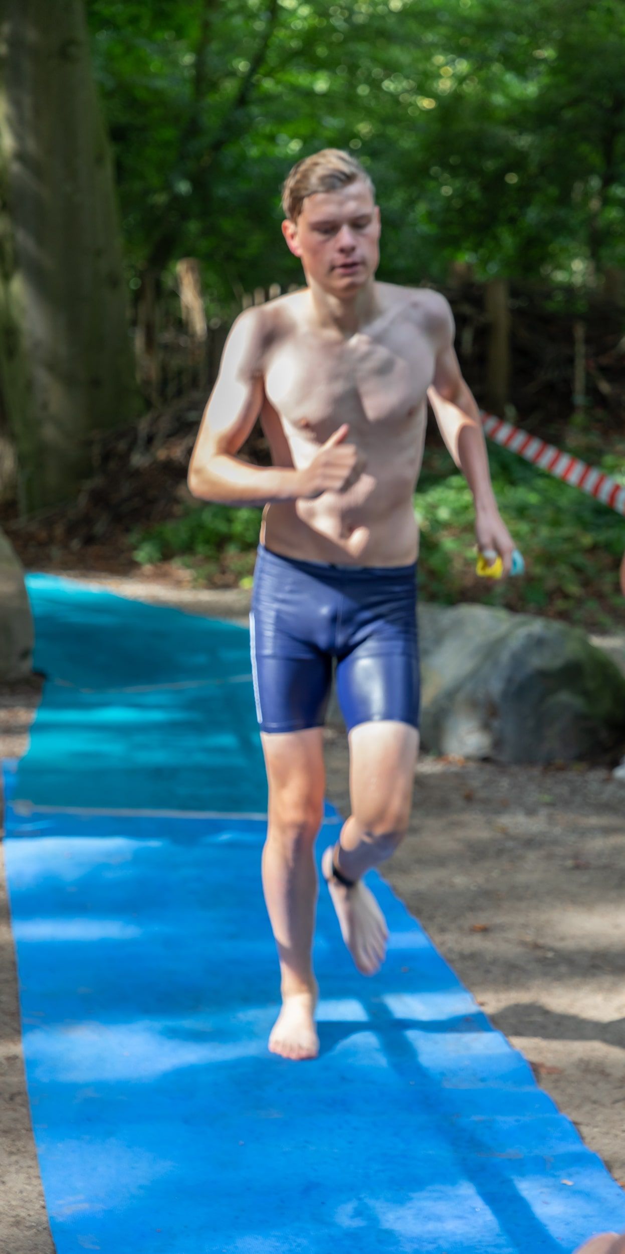 Een man zonder shirt rent op een blauwe mat in het bos.