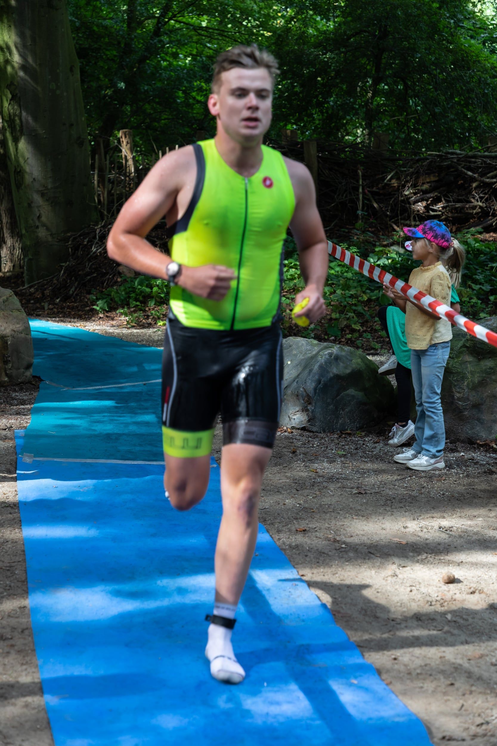 Een man in een geel tanktopje en een zwarte korte broek rent op een blauwe mat.