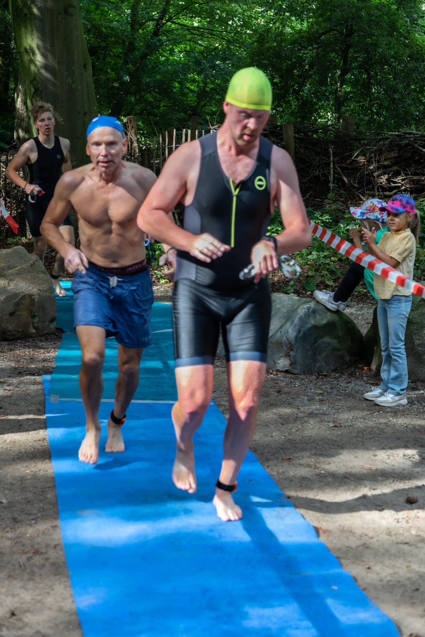 Twee mannen rennen op een blauwe mat in het bos.