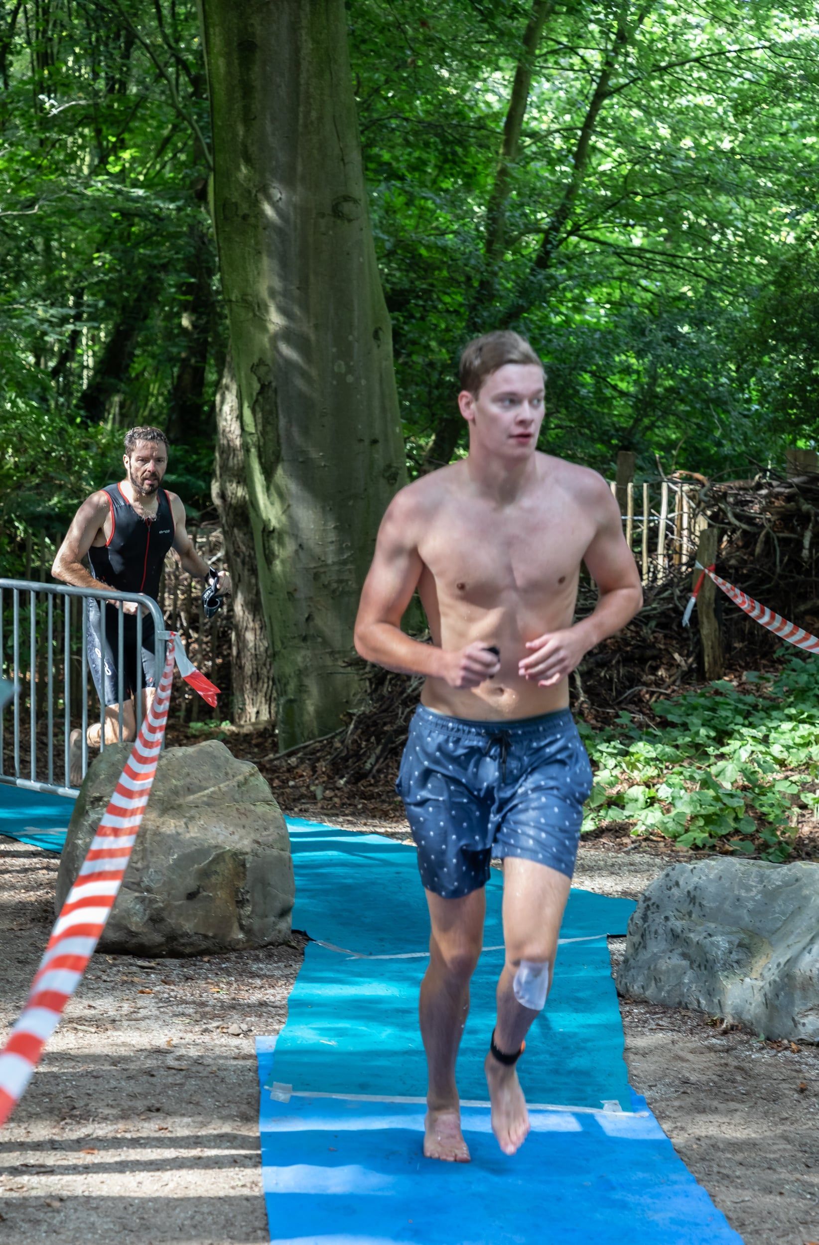 Een man zonder shirt rent op een blauwe mat in het bos.