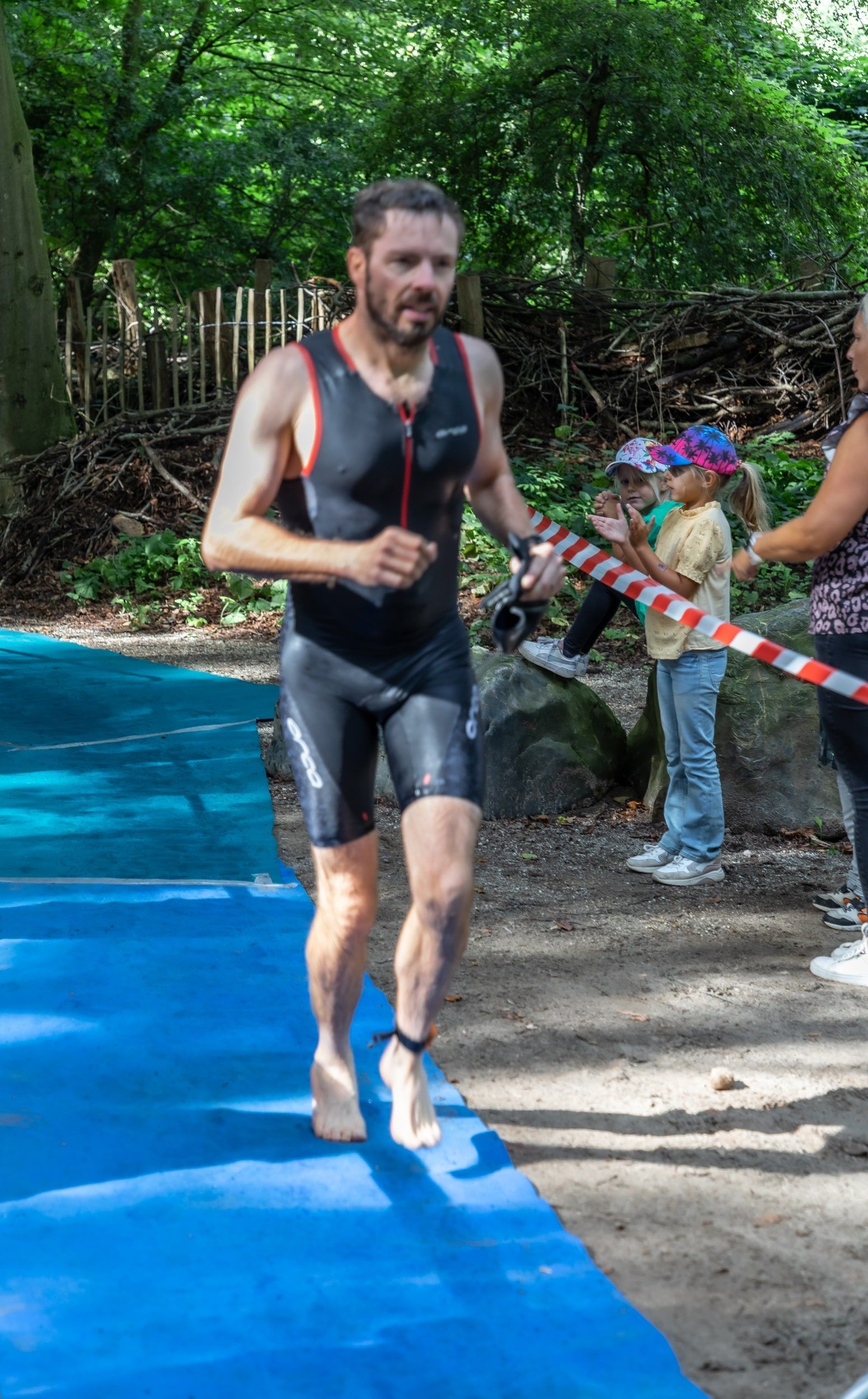 Een man in een wetsuit rent op een blauwe mat.