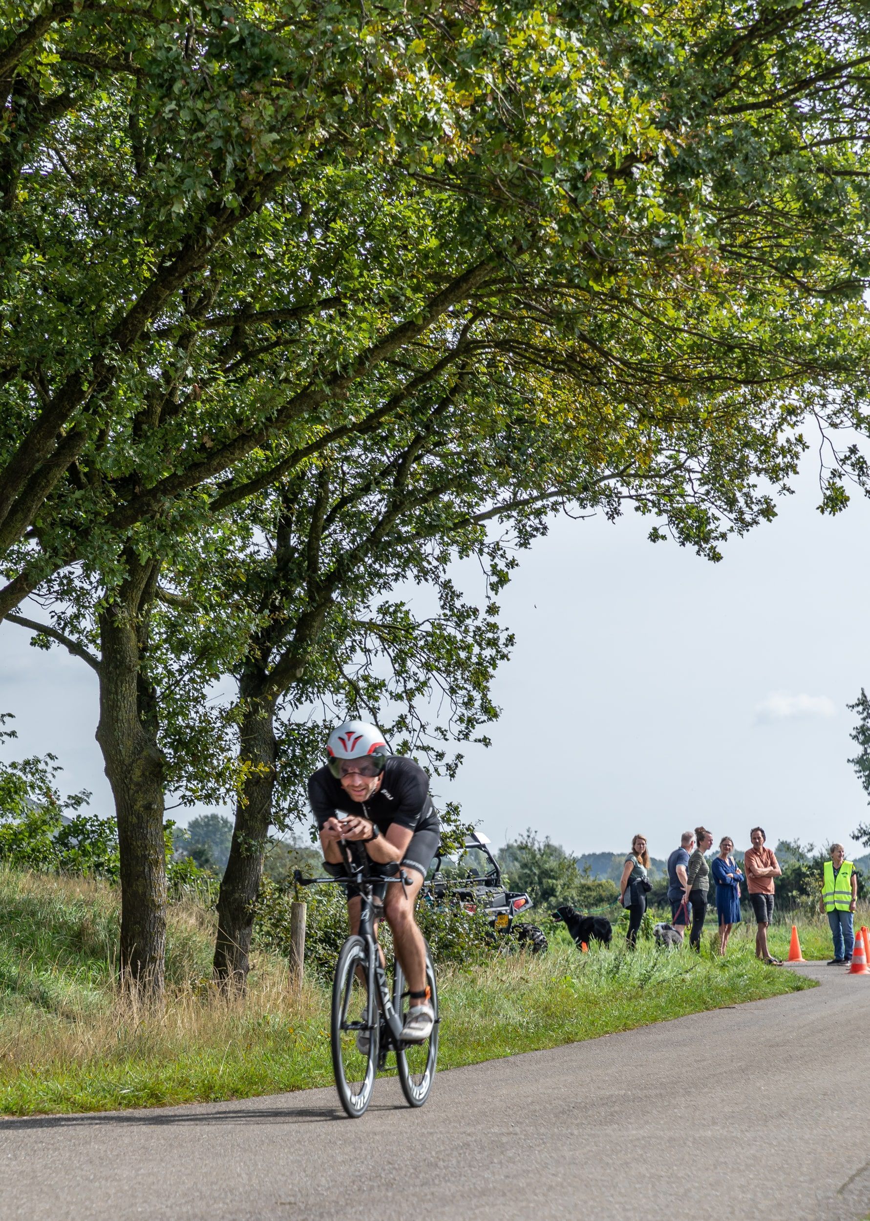 Een man fietst over een weg met bomen op de achtergrond.