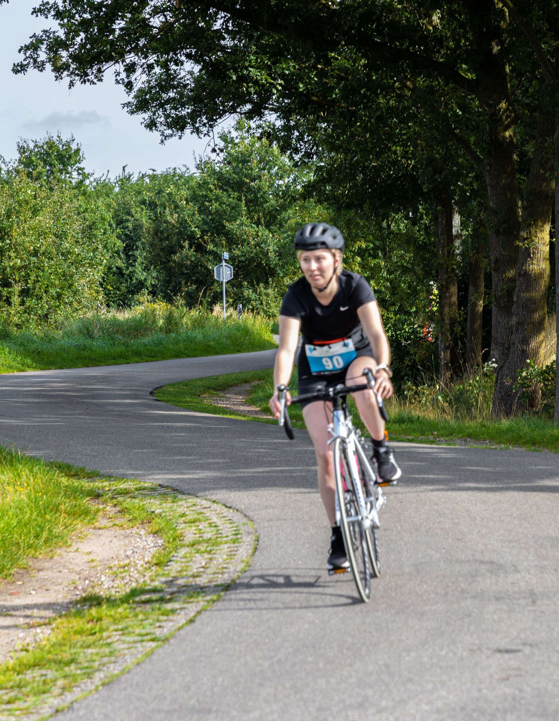 Een vrouw met een helm rijdt op een fiets over een weg