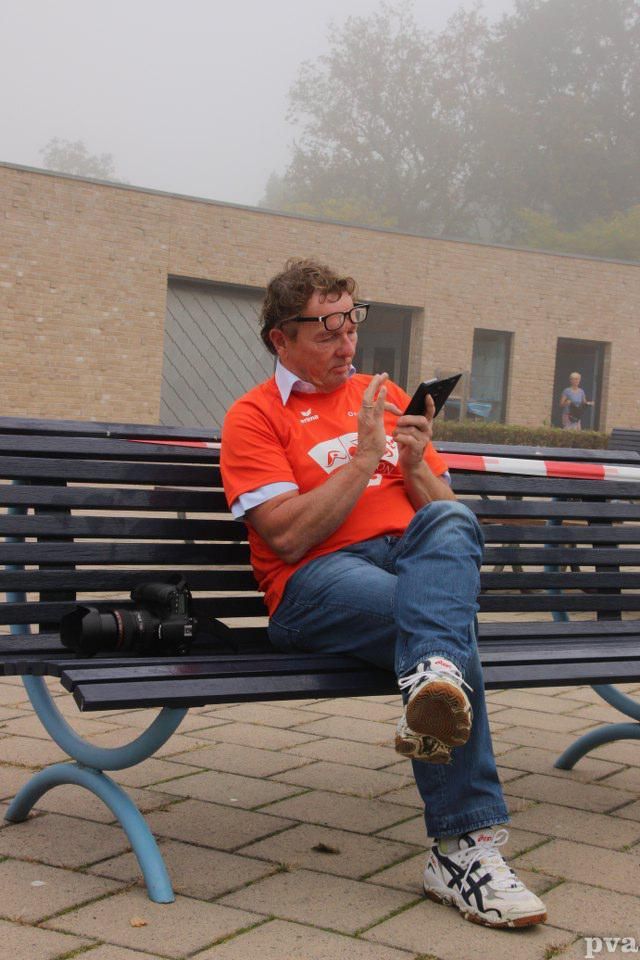 Triathlon Eibergen. Een man zit op een bankje en kijkt naar zijn telefoon