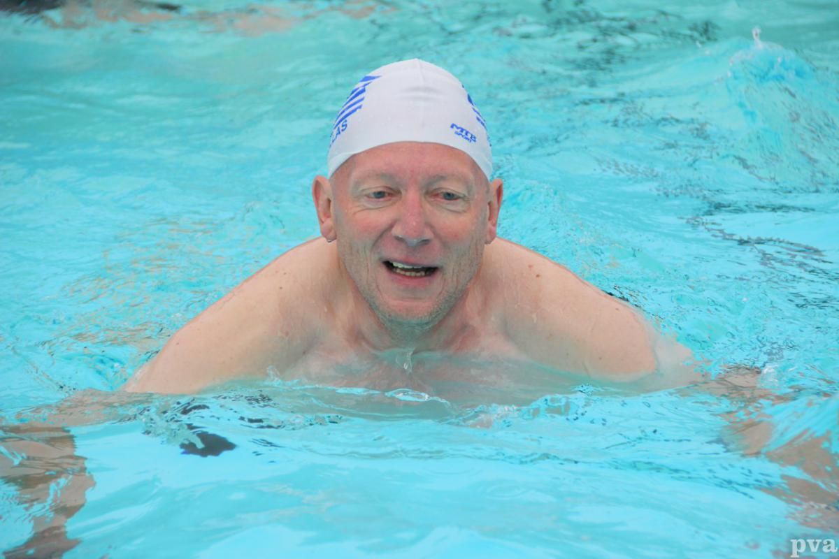 Triathlon Eibergen. Een oudere man zwemt in een zwembad met een badmuts op.
