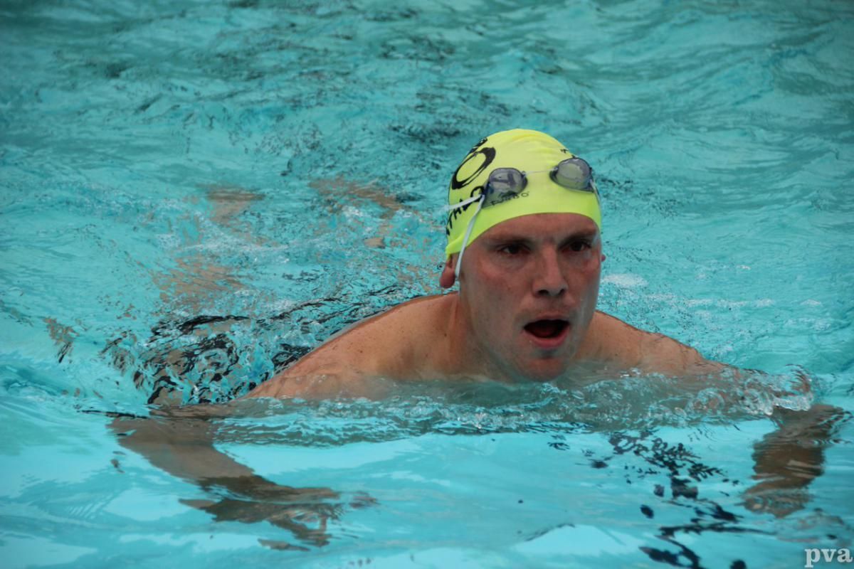 Triathlon Eibergen. Een man met een gele badmuts en een duikbril zwemt in een zwembad.