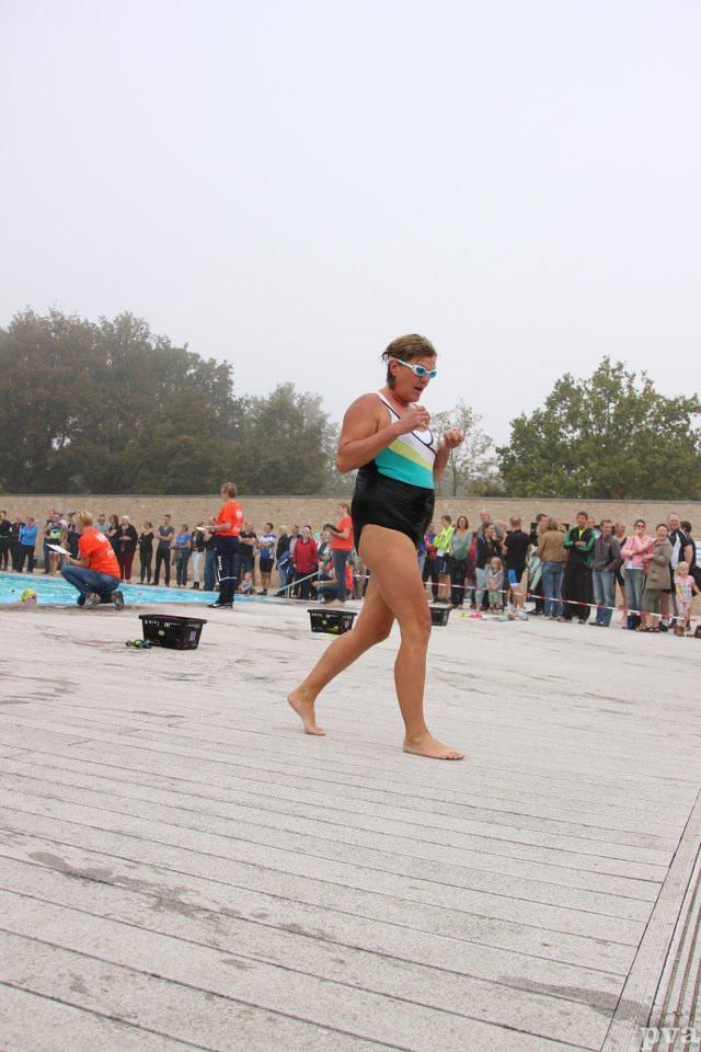 Triathlon Eibergen. Een vrouw in badpak loopt op blote voeten voor een menigte mensen.
