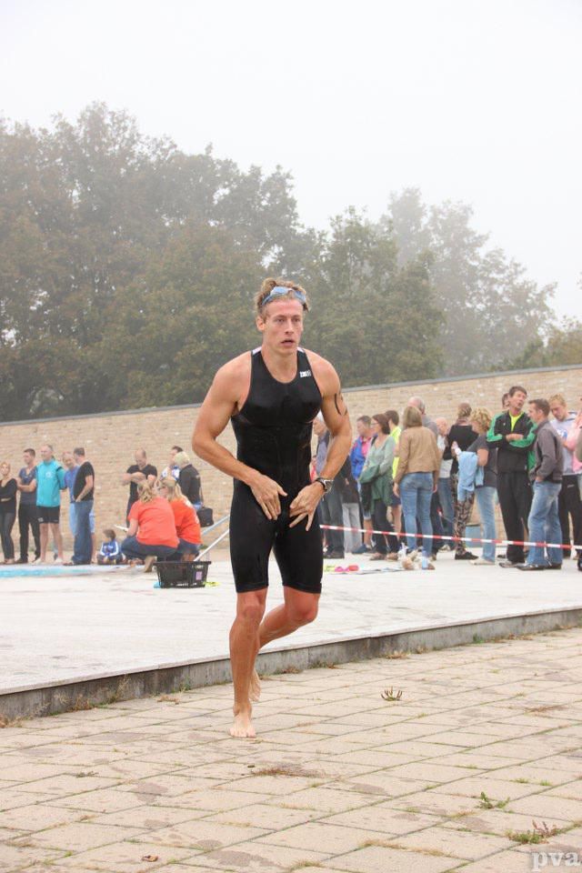 Triathlon Eibergen. Een man in een wetsuit rent voor een menigte uit.