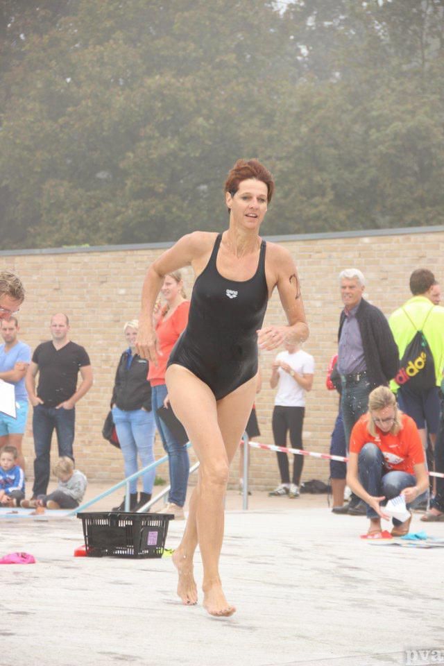 Triathlon Eibergen. Een vrouw in een zwart badpak rent op blote voeten voor een menigte uit.