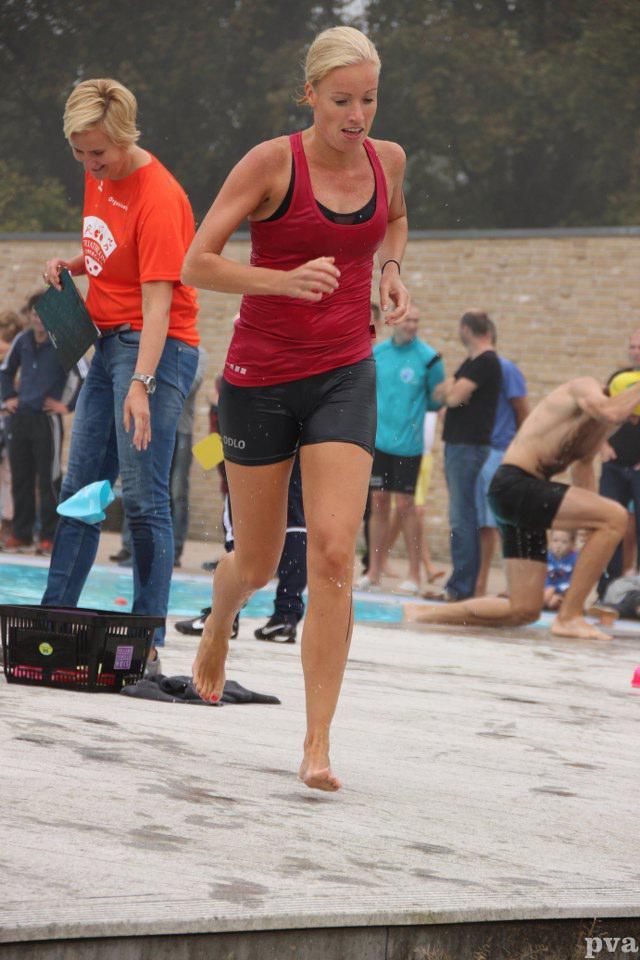 Triathlon Eibergen. Een vrouw in een rood tanktopje en zwarte shorts rent langs een zwembad