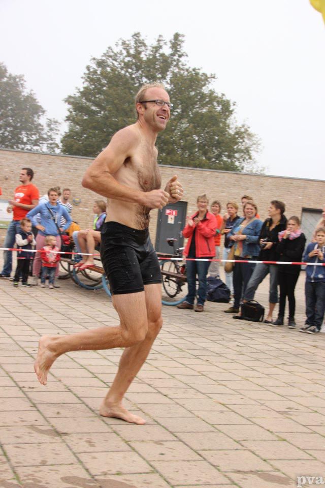 Triathlon Eibergen. Een man zonder shirt rent op blote voeten voor een menigte uit.