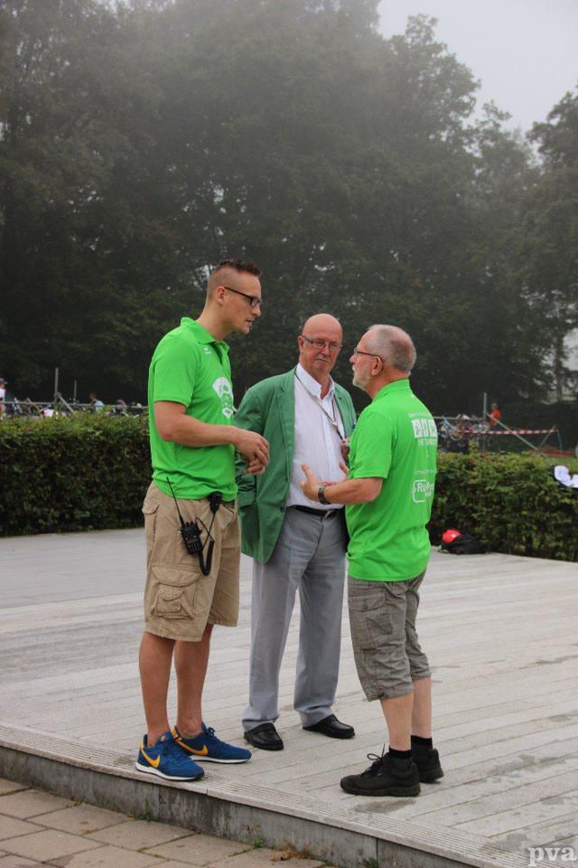 Triathlon Eibergen. Drie mannen in groene shirts staan ​​op de stoep met elkaar te praten.