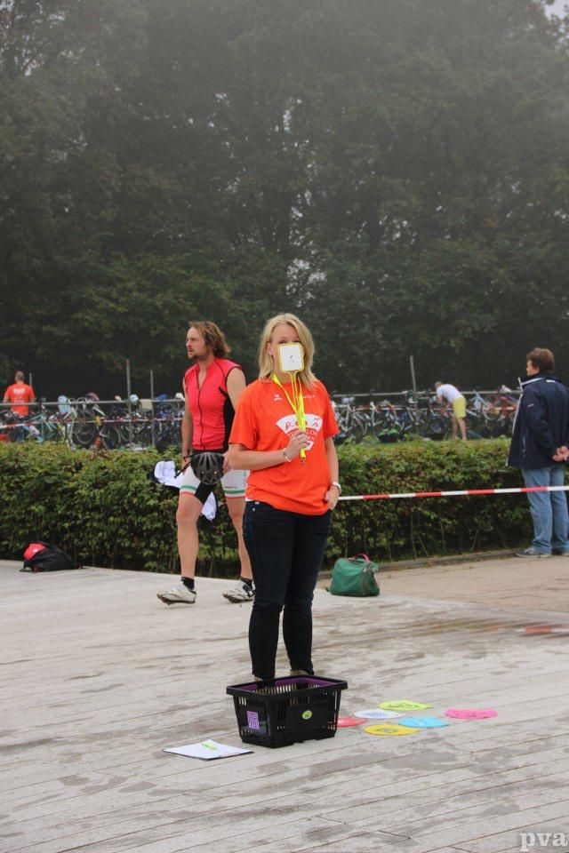 Triathlon Eibergen. Een vrouw in een oranje shirt houdt een stuk papier voor haar gezicht