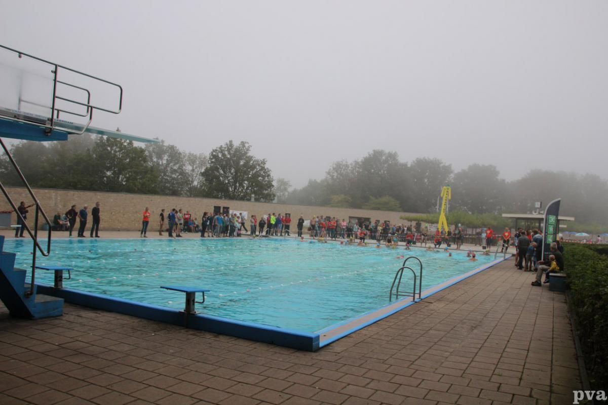 Triathlon Eibergen. Een groep mensen staat op een mistige dag rond een zwembad.