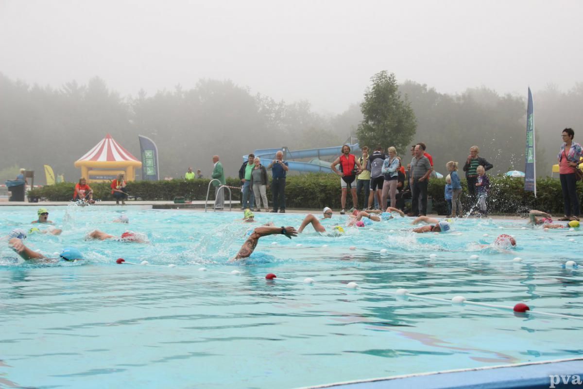 Triathlon Eibergen. Een groep mensen zwemt in een zwembad op een mistige dag.
