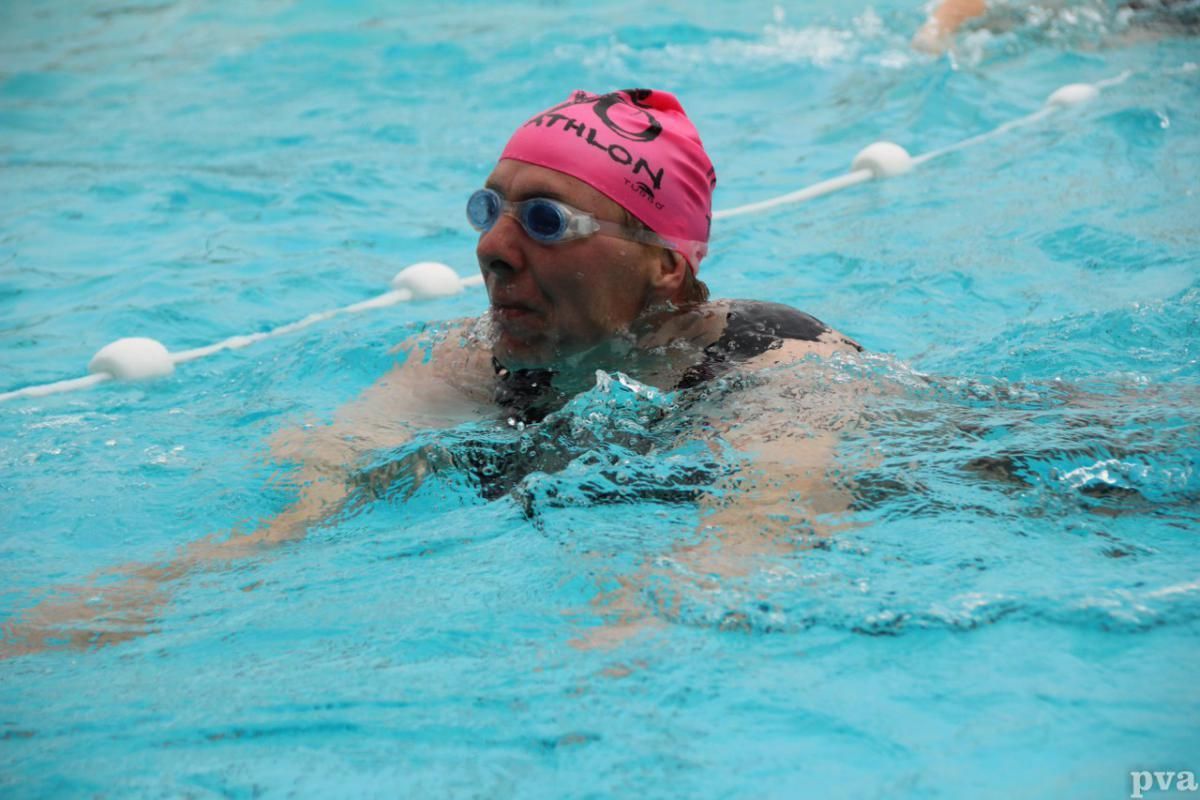Triathlon Eibergen. Een man met een roze badmuts en een zwembril zwemt in een zwembad.