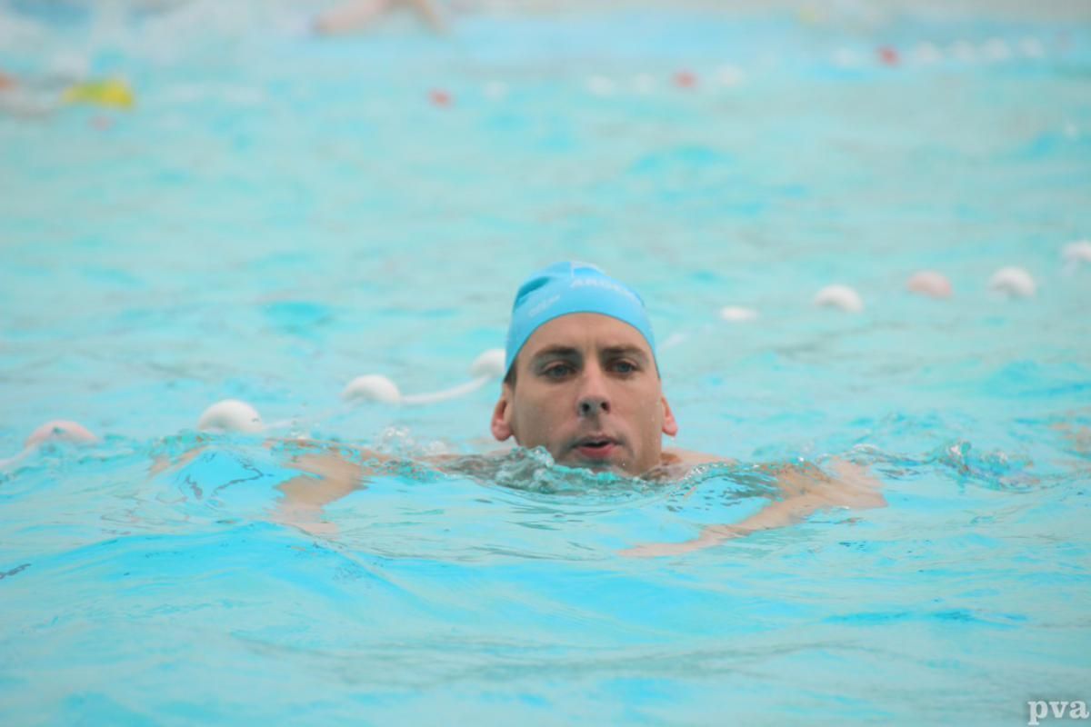 Triathlon Eibergen. Een man zwemt in een zwembad met een blauwe badmuts op.