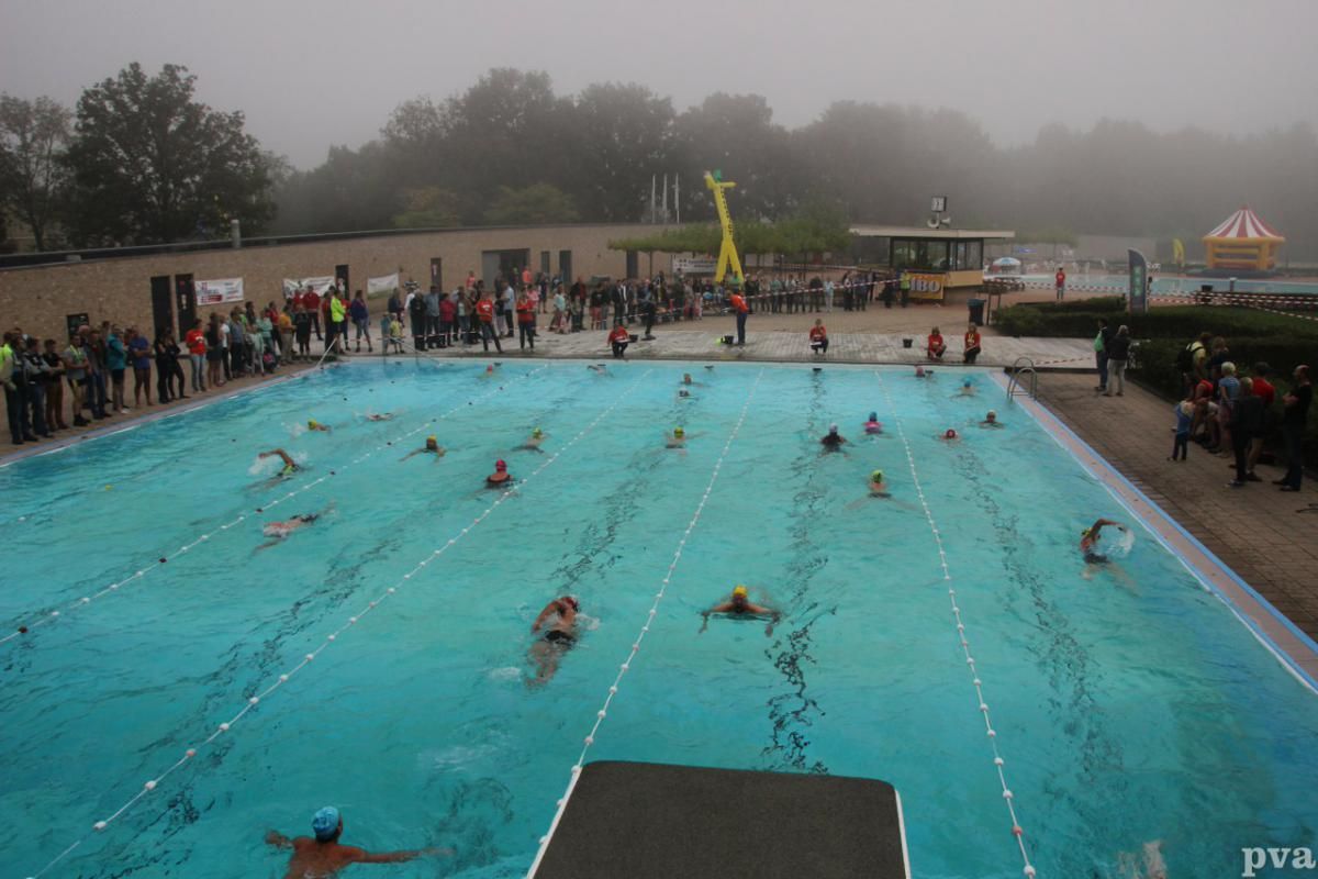 Triathlon Eibergen. Een groep mensen zwemt in een zwembad op een mistige dag.