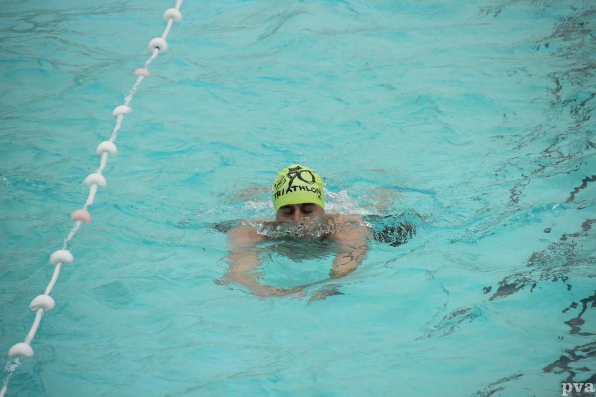 Triathlon Eibergen. Een man zwemt in een zwembad met een gele badmuts op.