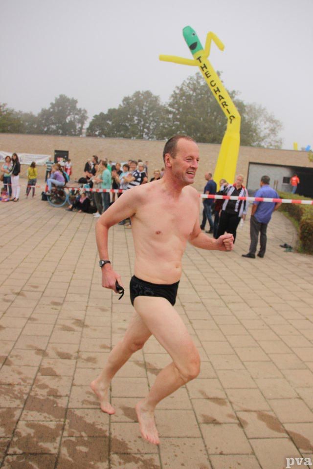 Triathlon Eibergen. Een man zonder shirt in een zwarte zwembroek rent op een stoep