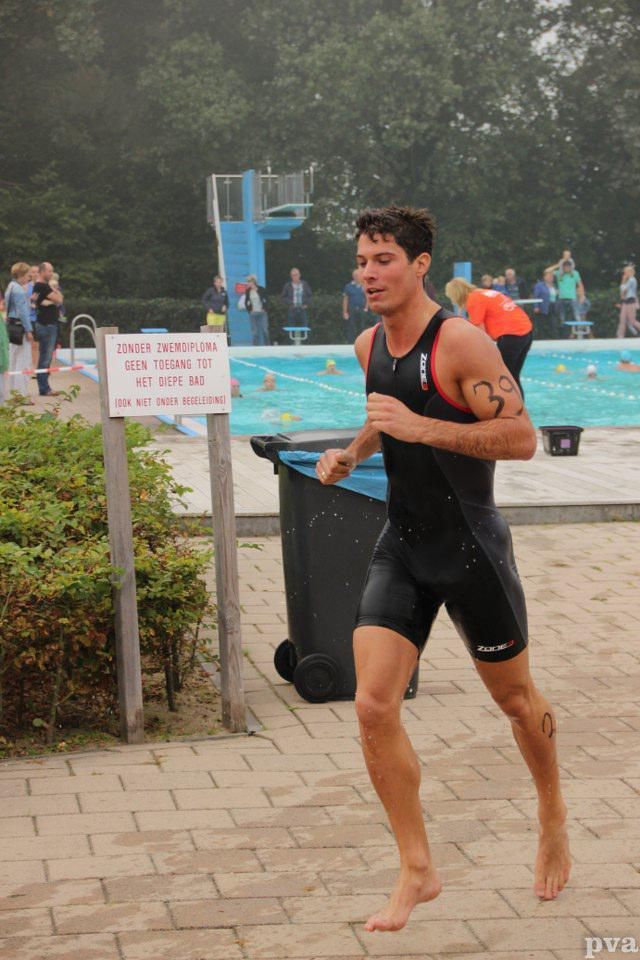 Triathlon Eibergen. Een man in een wetsuit rent voor een zwembad.