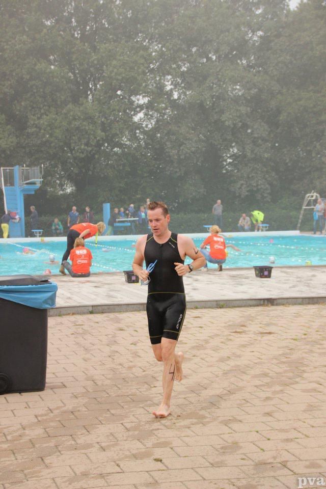 Triathlon Eibergen. Een man rent op blote voeten voor een zwembad.
