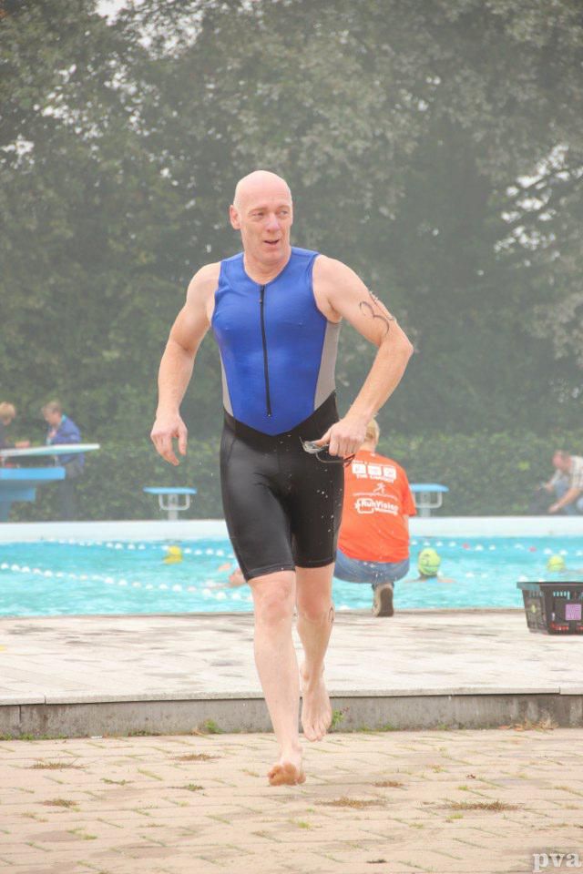 Triathlon Eibergen. Een man in een blauw tanktopje en een zwarte korte broek rent naar een zwembad.