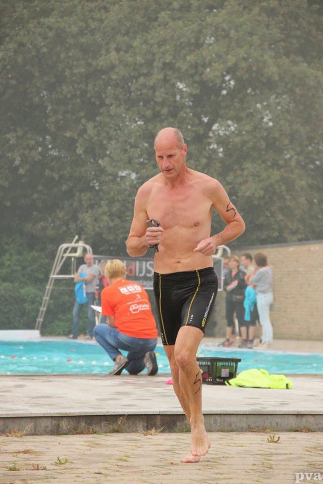 Triathlon Eibergen. Een man zonder shirt rent voor een zwembad.