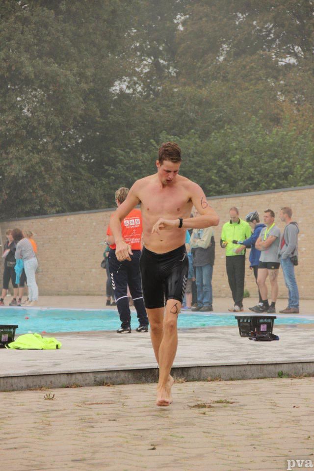 Triathlon Eibergen. Een man zonder shirt rent op blote voeten voor een zwembad.