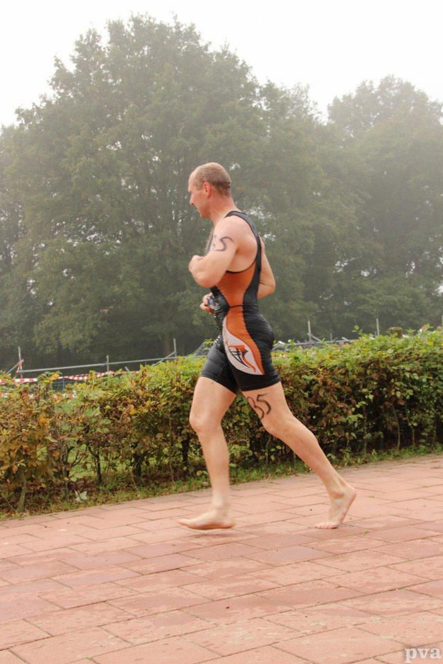 Triathlon Eibergen. Een man rent op blote voeten over een stoep van bakstenen.