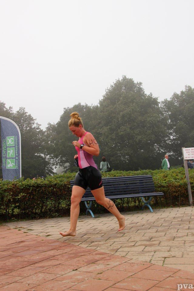 Triathlon Eibergen. Een vrouw rent op blote voeten over een stoep van bakstenen.