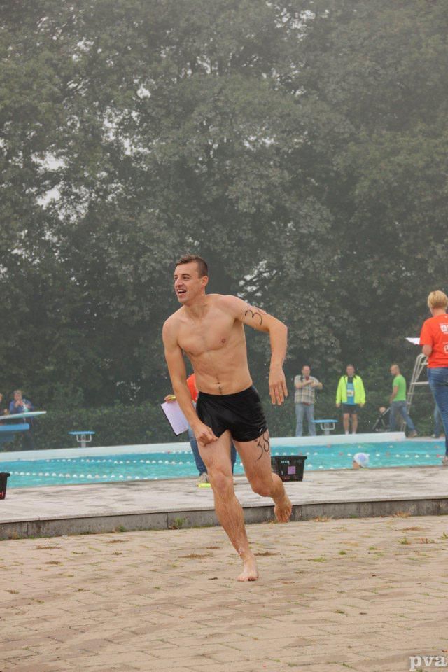 Triathlon Eibergen. Een man zonder shirt rent door het zand bij een zwembad.
