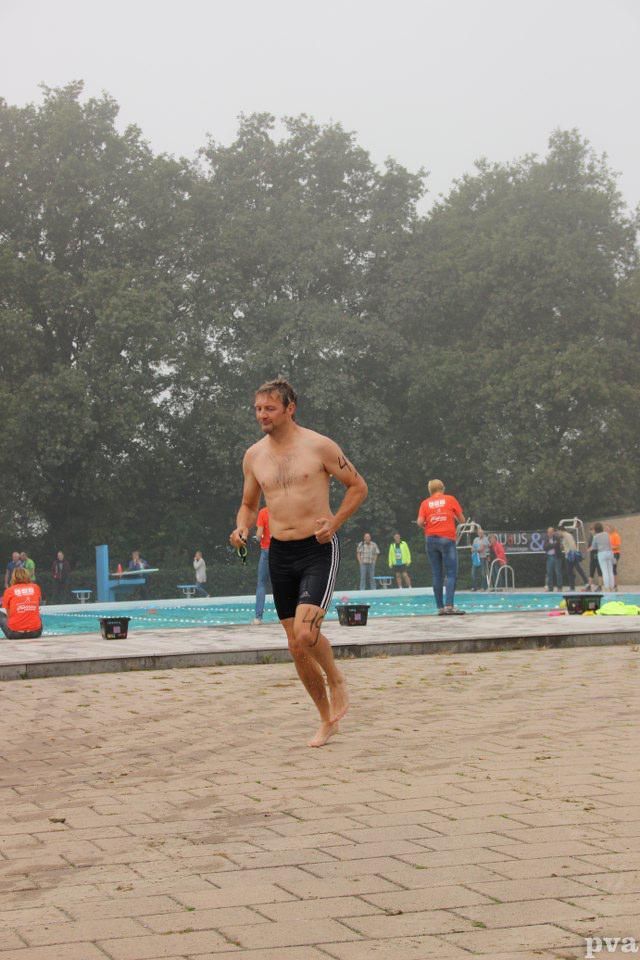 Triathlon Eibergen. Een man zonder shirt rent op blote voeten voor een zwembad.