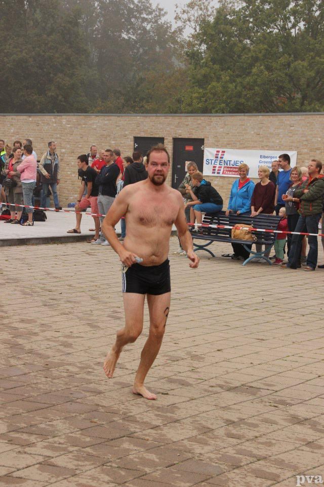 Triathlon Eibergen. Een man zonder shirt in een zwarte zwembroek rent voor een menigte mensen uit.