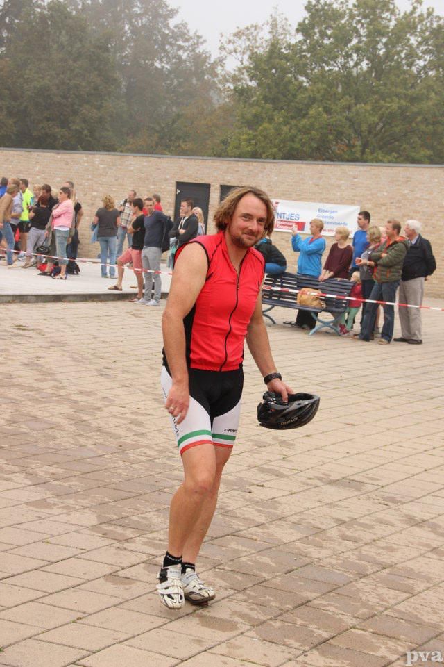 Triathlon Eibergen. Een man in een rood shirt houdt een helm vast voor een menigte mensen.