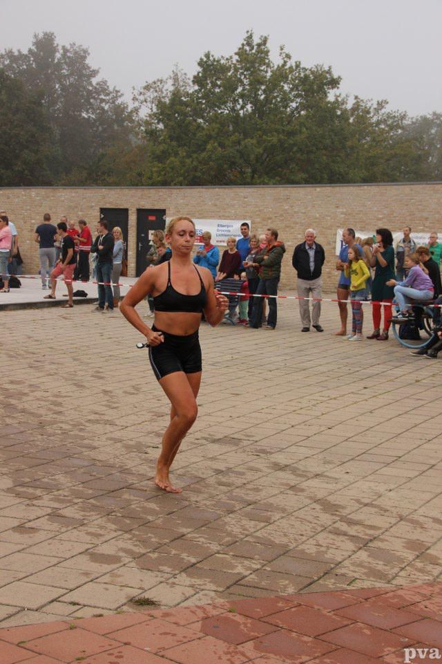 Triathlon Eibergen. Een vrouw rent op blote voeten over een stoep van bakstenen, voor een menigte mensen.