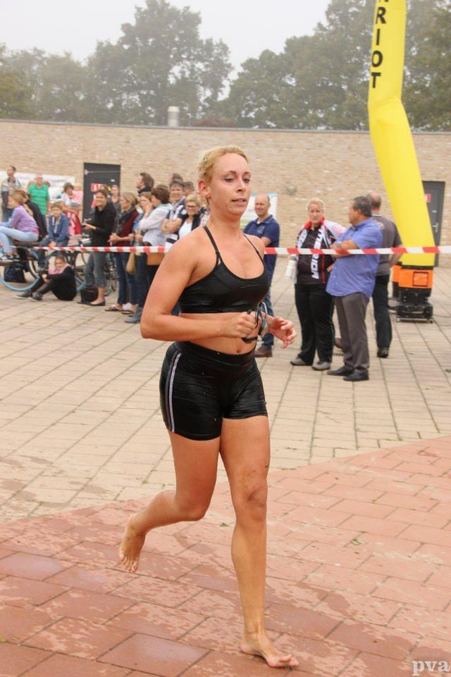 Triathlon Eibergen. Een vrouw in een zwart topje en een korte broek rent op blote voeten voor een menigte.
