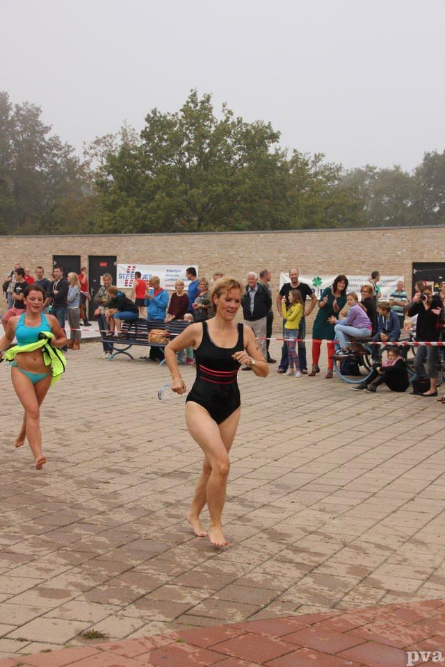 Triathlon Eibergen. Twee vrouwen in badpakken rennen op de stoep voor een menigte.