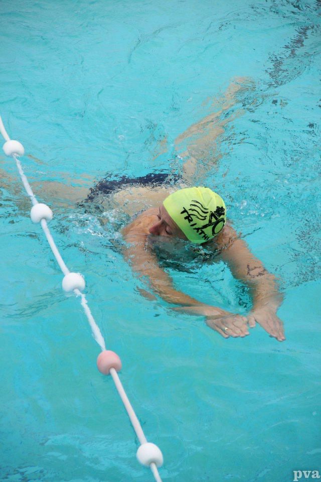 Triathlon Eibergen. Een man zwemt in een zwembad met een gele badmuts op.