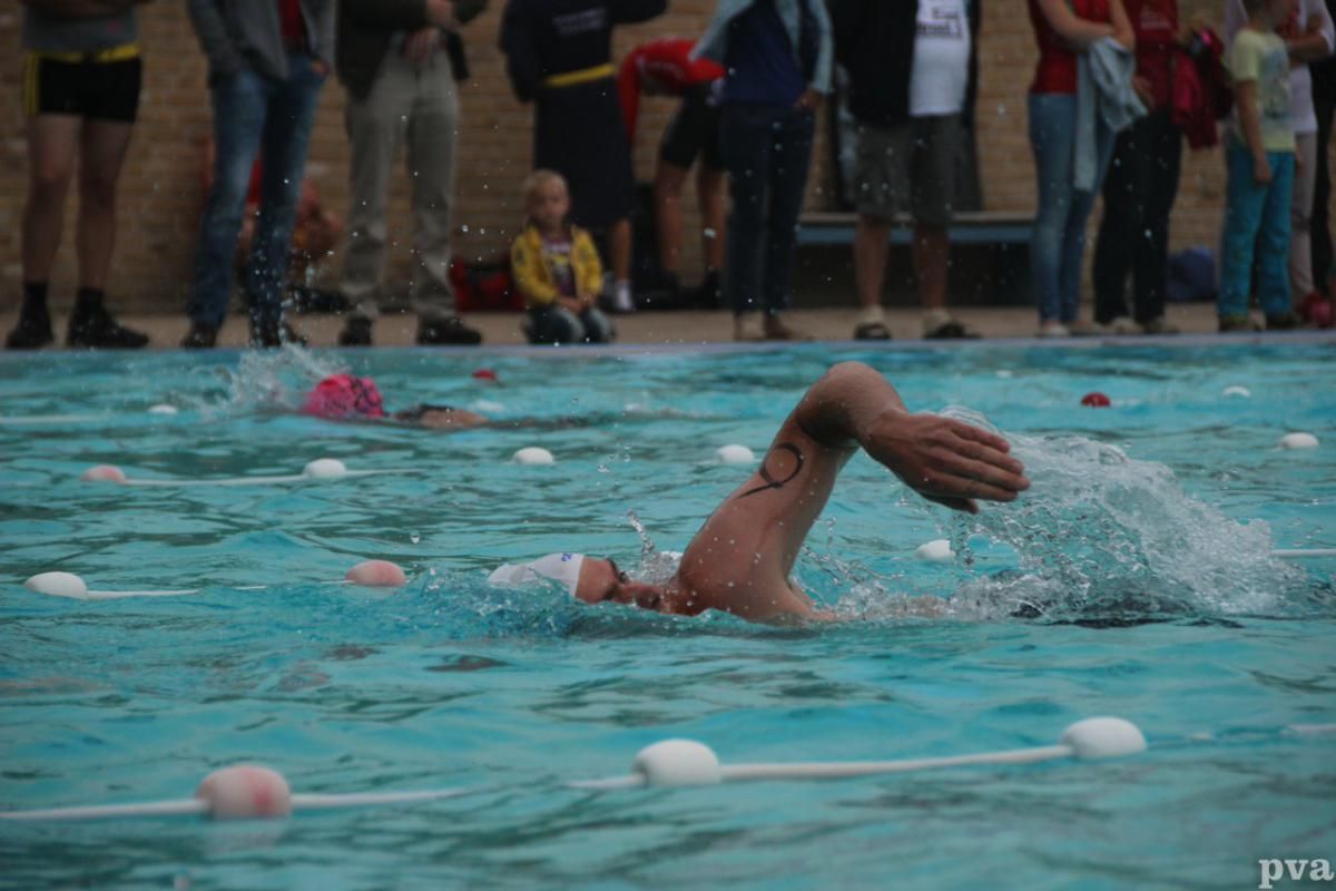 Triathlon Eibergen. Een man zwemt in een zwembad terwijl er een menigte toekijkt.