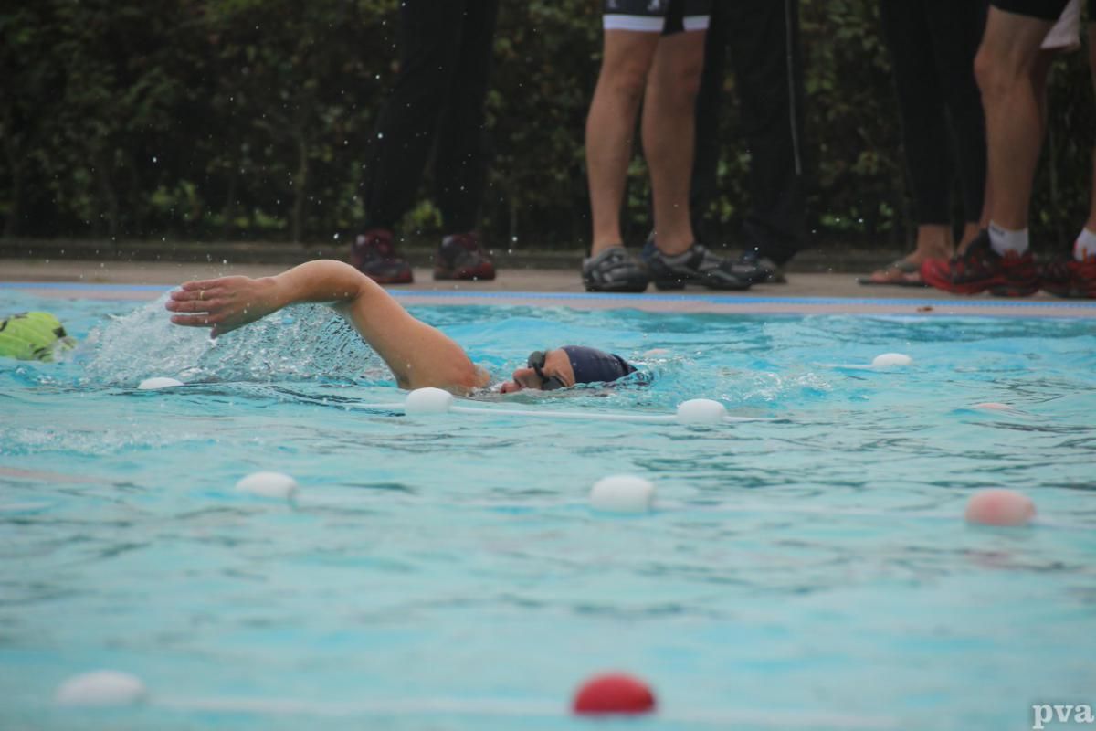 Triathlon Eibergen. Iemand zwemt in een zwembad terwijl een groep mensen toekijkt.